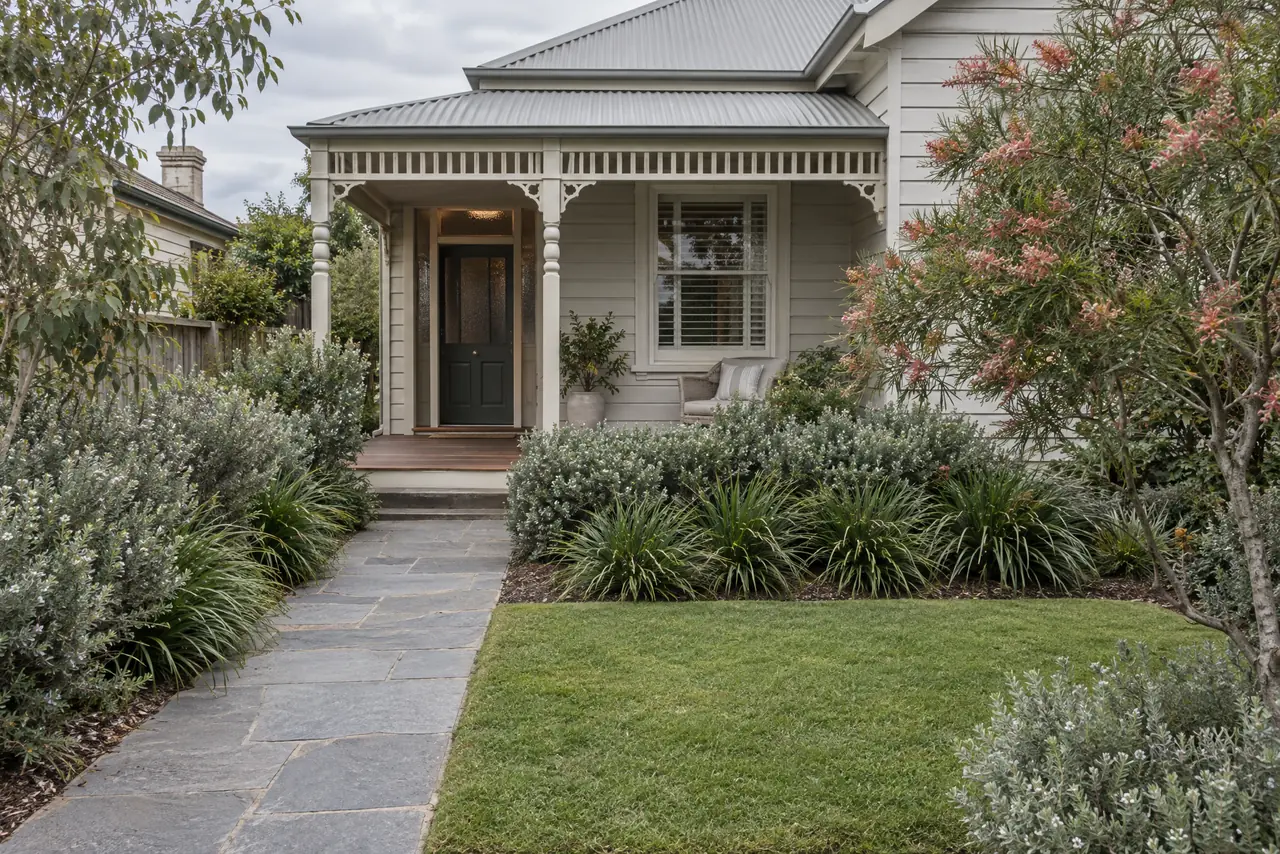 A neat native front garden with a bluestone path, edged lawn and trimmed shrubs.